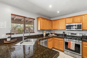Una cocina moderna con encimeras de granito, electrodomésticos de acero inoxidable, armarios de madera y una ventana con persianas.