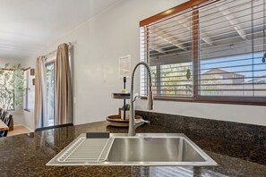 Una cocina moderna con un lavamanos de acero inoxidable, estufa integrada y ventana con persianas.