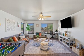 A living room with a sofa, coffee table, ottoman, and a foosball table.