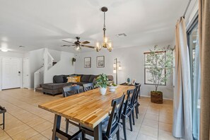 Un espacio habitable moderno con comedor, ventilador de techo y un amplio ventanal con cortinas.
