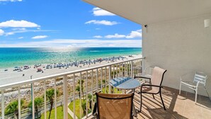 Een balkon met uitzicht op een strand, een tafel en twee stoelen.