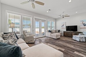 A spacious living room with a large sectional sofa, a recliner, a TV on a wooden cabinet, and a ceiling fan. - 4101 Choctaw St (Panama City Beach)
