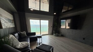 A modern living room with a sofa, armchairs, a coffee table, and a TV. There is a balcony with a view of the sea. - The Summit 1305 (Panama City Beach)