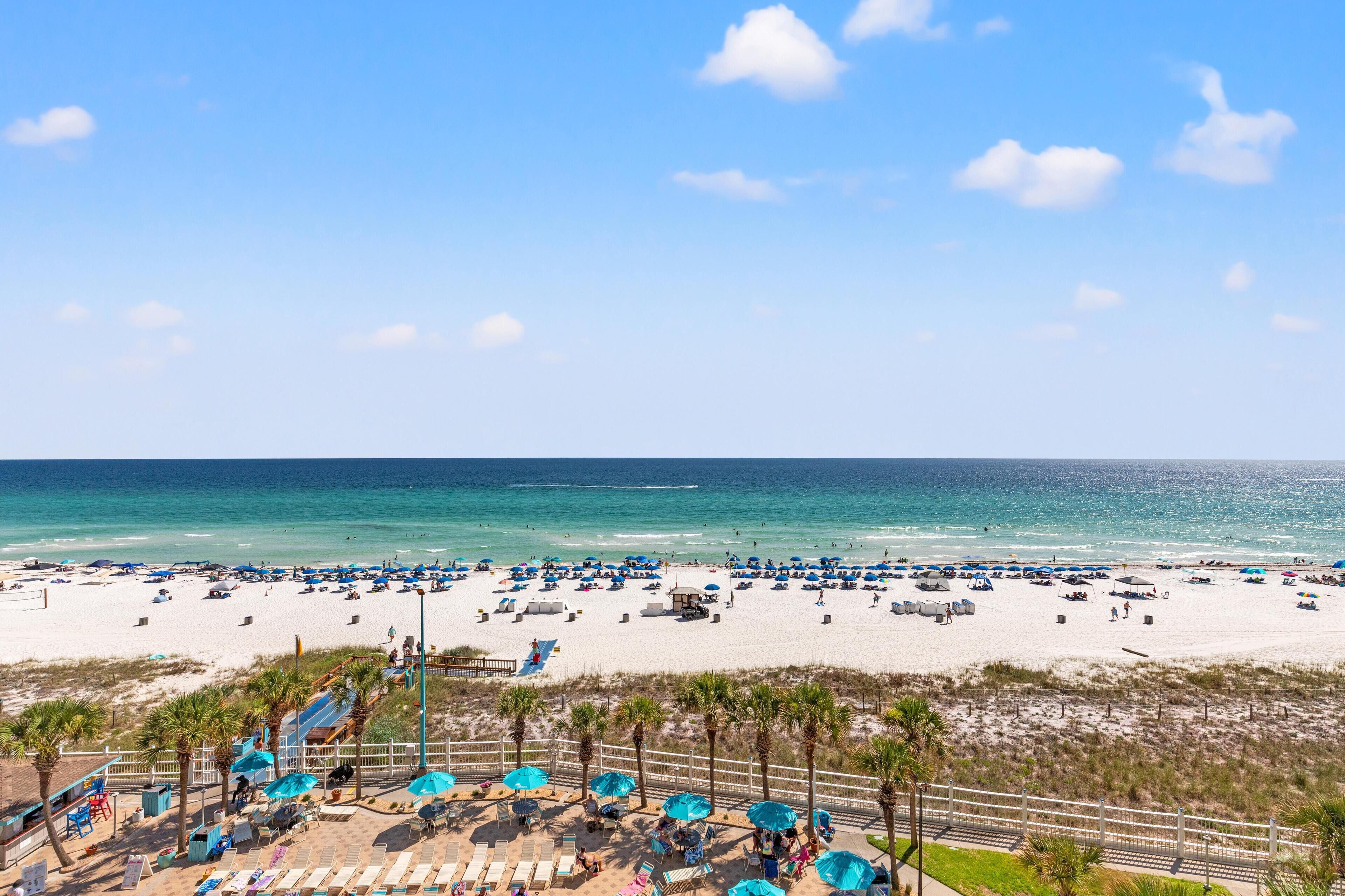 A beach with numerous umbrellas and lounge chairs, a clear sky, and a calm sea.