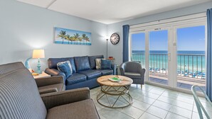 A living room with a blue sofa, a round coffee table, and a view of the beach through large sliding doors. - The Summit 712 (Panama City Beach)