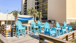 A deck with blue Adirondack chairs and a blue canopy, overlooking a building with multiple balconies. - Top of The Gulf 306 (Panama City Beach)