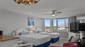 A hotel room with two beds, a TV, a desk, and a view of the beach. - Top of The Gulf 306 (Panama City Beach)