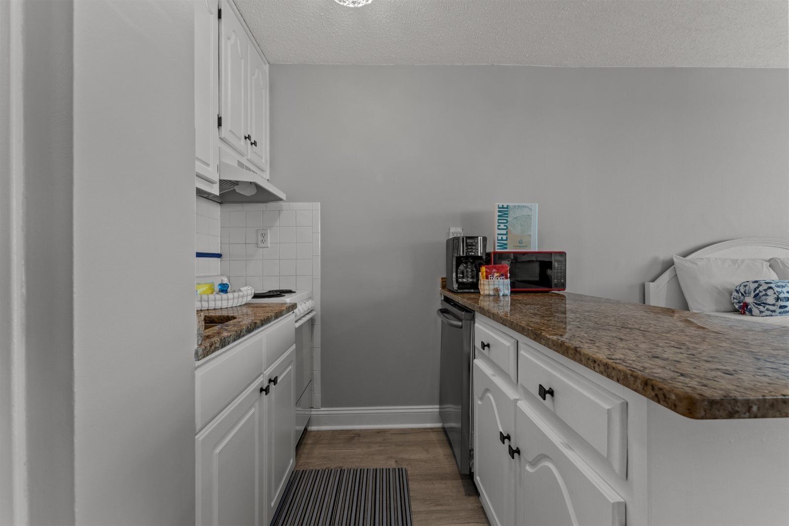A compact kitchen with white cabinetry, a granite countertop, a coffee maker, and a microwave.