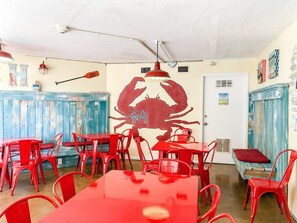 A restaurant interior with red tables and chairs, a large crab mural on the wall, and a white door. - Top of The Gulf 306 (Panama City Beach)