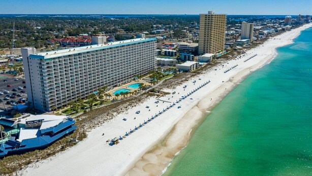A coastal hotel with a large building, a beach, and a pool area.