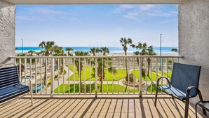 A balcony with a view of the beach, palm trees, and a clear sky.