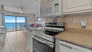 A modern kitchen with stainless steel appliances, a granite countertop, and a view of the ocean through a sliding glass door. - The Summit 1213 (Panama City Beach)