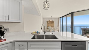 A modern kitchen with a built-in dishwasher, a coffee maker, and a dining area with a view of the ocean.