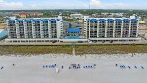 A beachfront hotel with multiple floors, a swimming pool, and a beach area with sun loungers.
