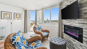 Una sala de estar moderna con un televisor grande, muebles de mimbre y vista al mar.