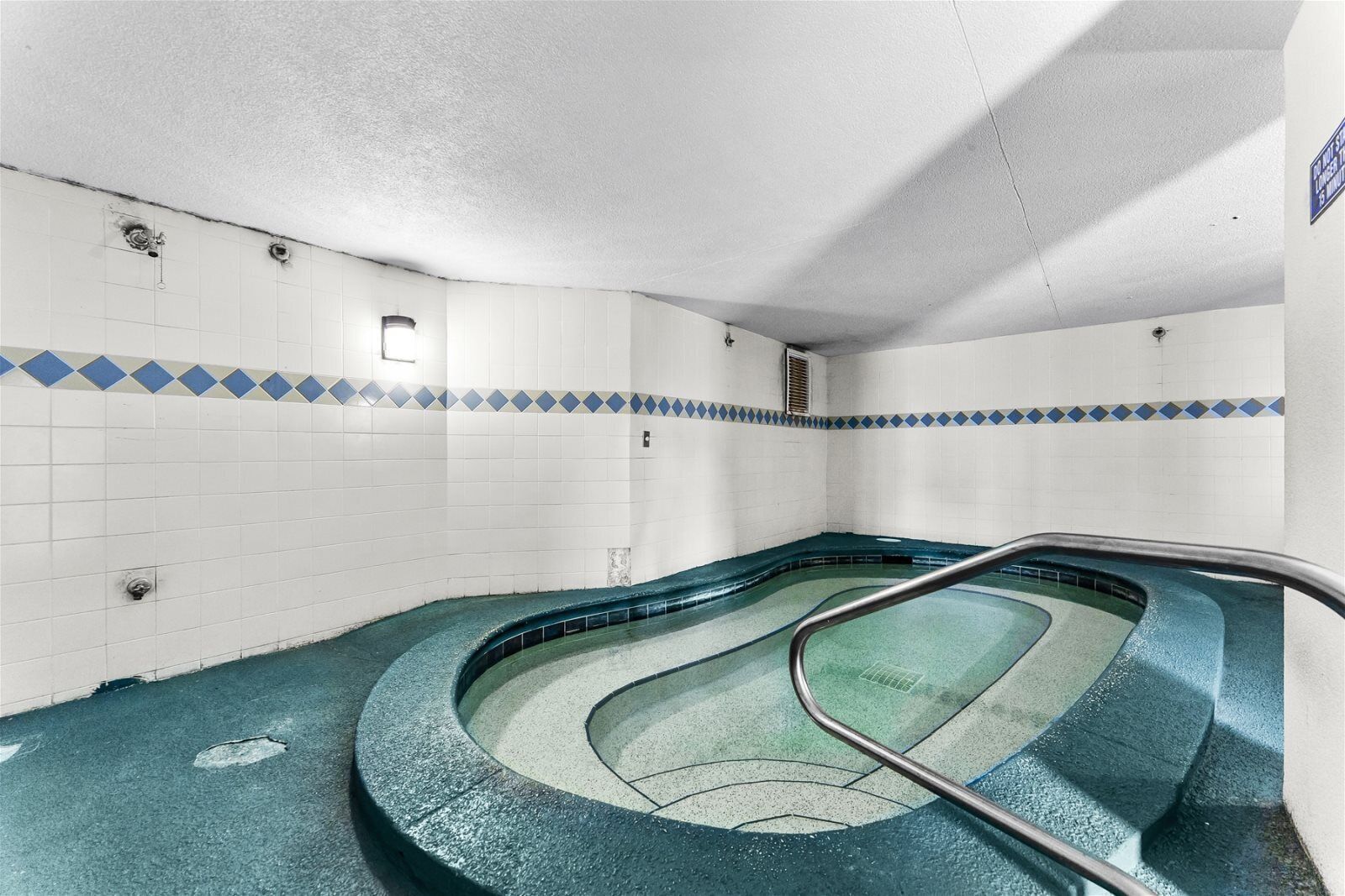 Ein Schwimmbecken mit gebogener Form, gefliesten Wänden und einem Metallgeländer.