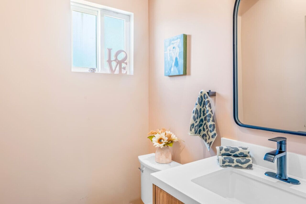 Un bagno con un lavandino bianco, uno specchio, un asciugamano e un vaso con fiori.
