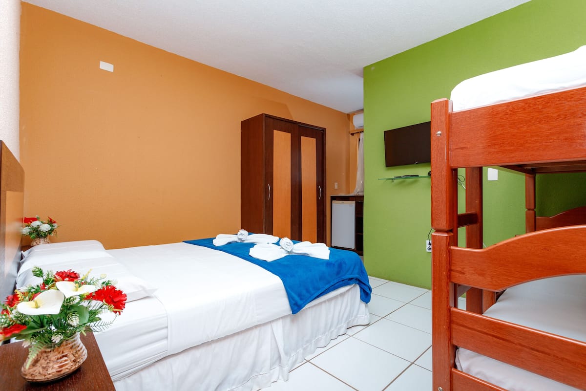 A hotel room with two beds, a wooden wardrobe, a green wall, and a small TV.
