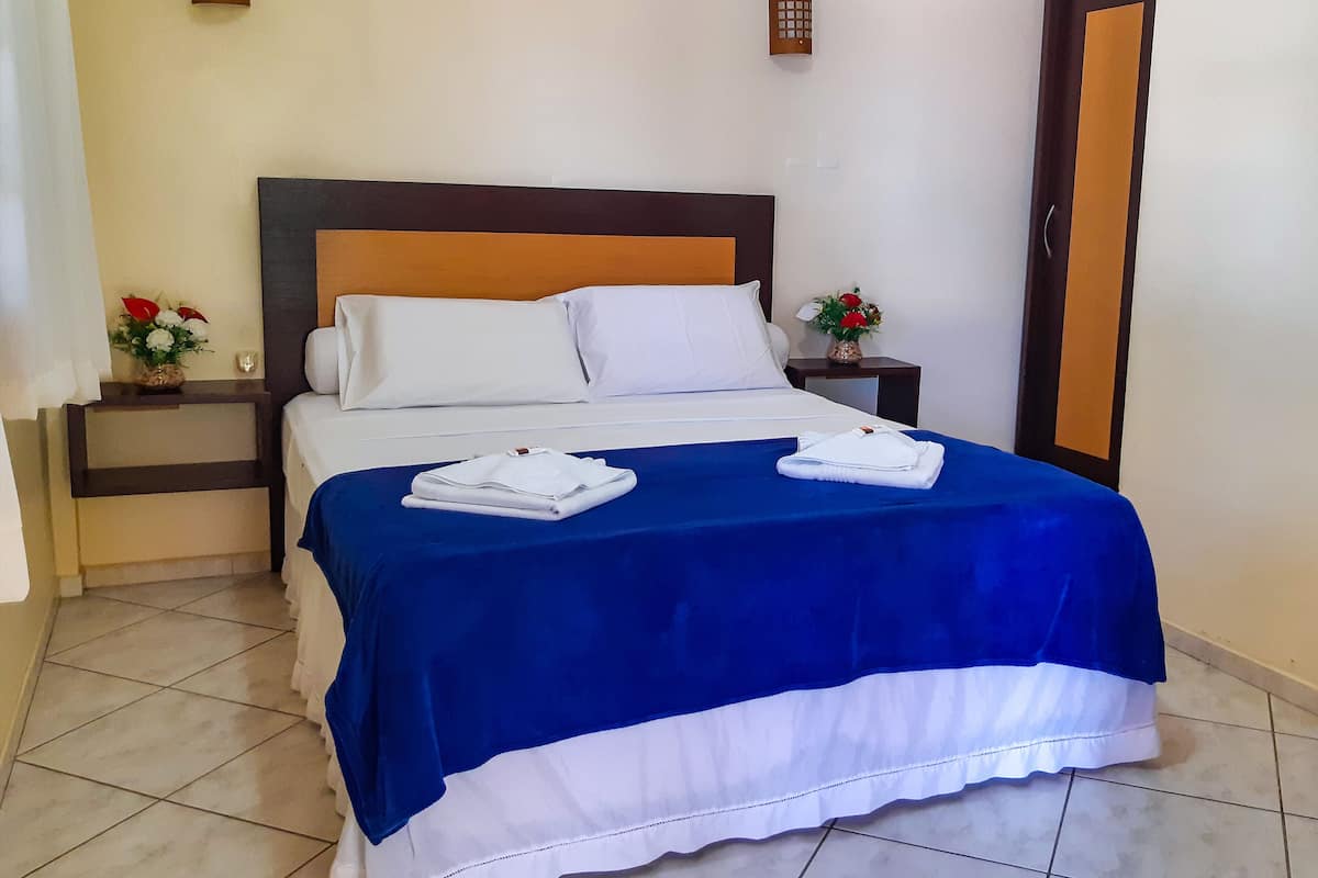 A neatly made bed with white and blue bedding, two bedside tables with lamps, and a door to the right.