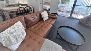 Una sala de estar moderna con un sofá de cuero marrón, una mesa de centro negra y una zona de comedor con una mesa y sillas de madera.