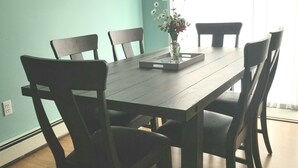 A dining room with a wooden table and six chairs, a vase with flowers, and a clock on the wall. - Riverview Home in Milbridge Maine (Milbridge)