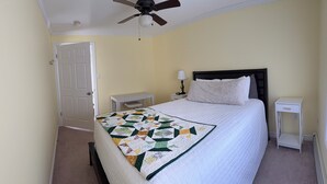 A bedroom with a bed, a nightstand, a lamp, a ceiling fan, and a door. - Riverview Home in Milbridge Maine (Milbridge)