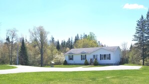 A single-story house with a front porch, surrounded by a well-maintained lawn and trees. - Riverview Home in Milbridge Maine (Milbridge)