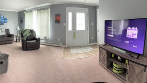 A living room with a flat-screen TV, grey sofas, a coffee table, and a fireplace. - Riverview Home in Milbridge Maine (Milbridge)
