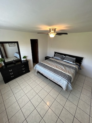 Une chambre à coucher avec un lit, une commode, un miroir et un ventilateur de plafond.