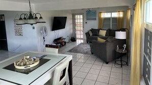 Sala de estar com sofá, mesa de jantar com centro de mesa decorativo, TV fixada na parede e ventilador de teto.