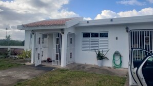 Um edifício branco com telhado ladrilhado, entrada com portão e um pequeno alpendre.