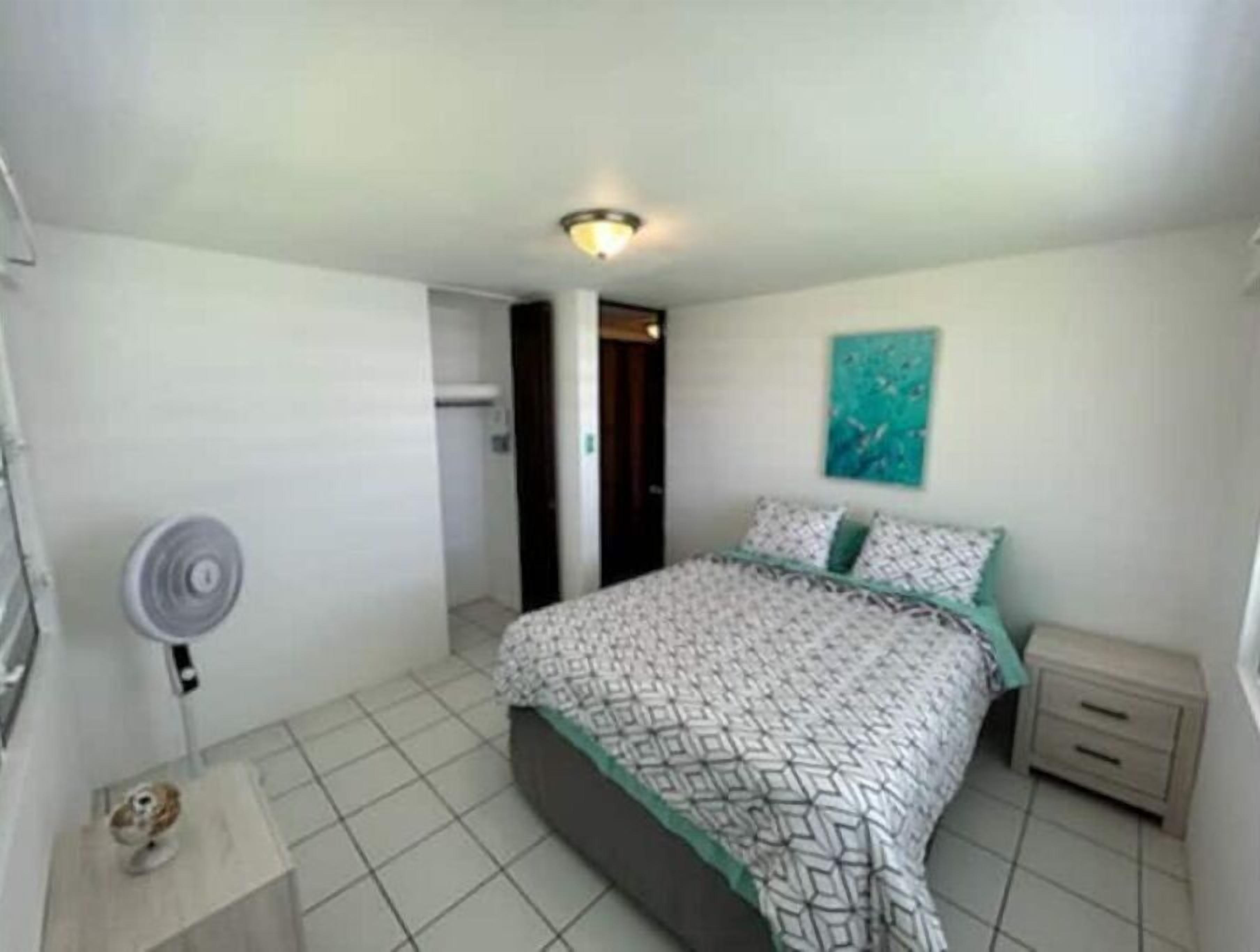 Ein Schlafzimmer mit Bett, Nachttisch, Wandbild und Deckenventilator.