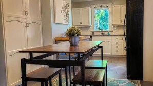 A modern kitchen with white cabinets, a wooden dining table with benches, and a potted plant on the table. - Beautiful 3 bedroom century home steps from uptown (Waterloo)