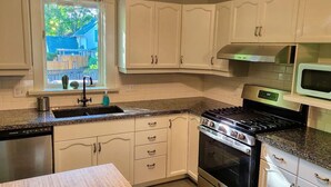A kitchen with white cabinets, a stainless steel stove, a microwave, and a window with a view of a backyard. - Beautiful 3 bedroom century home steps from uptown (Waterloo)