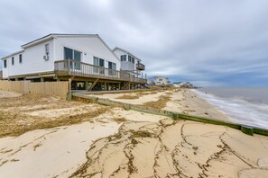 A beachfront house with a wooden deck and a balcony, situated on a sandy beach with visible tide marks. - Delaware Bay & Sunset Views: Cape May Cottage (Cape May Court House)