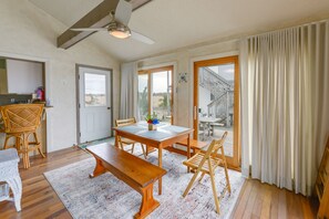 A dining area with a wooden table, benches, and chairs. There is a ceiling fan, a window with curtains, and a view of a staircase leading outside. - Delaware Bay & Sunset Views: Cape May Cottage (Cape May Court House)