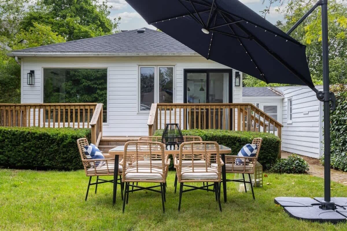 A house with a deck, a dining table with chairs, and a large umbrella.