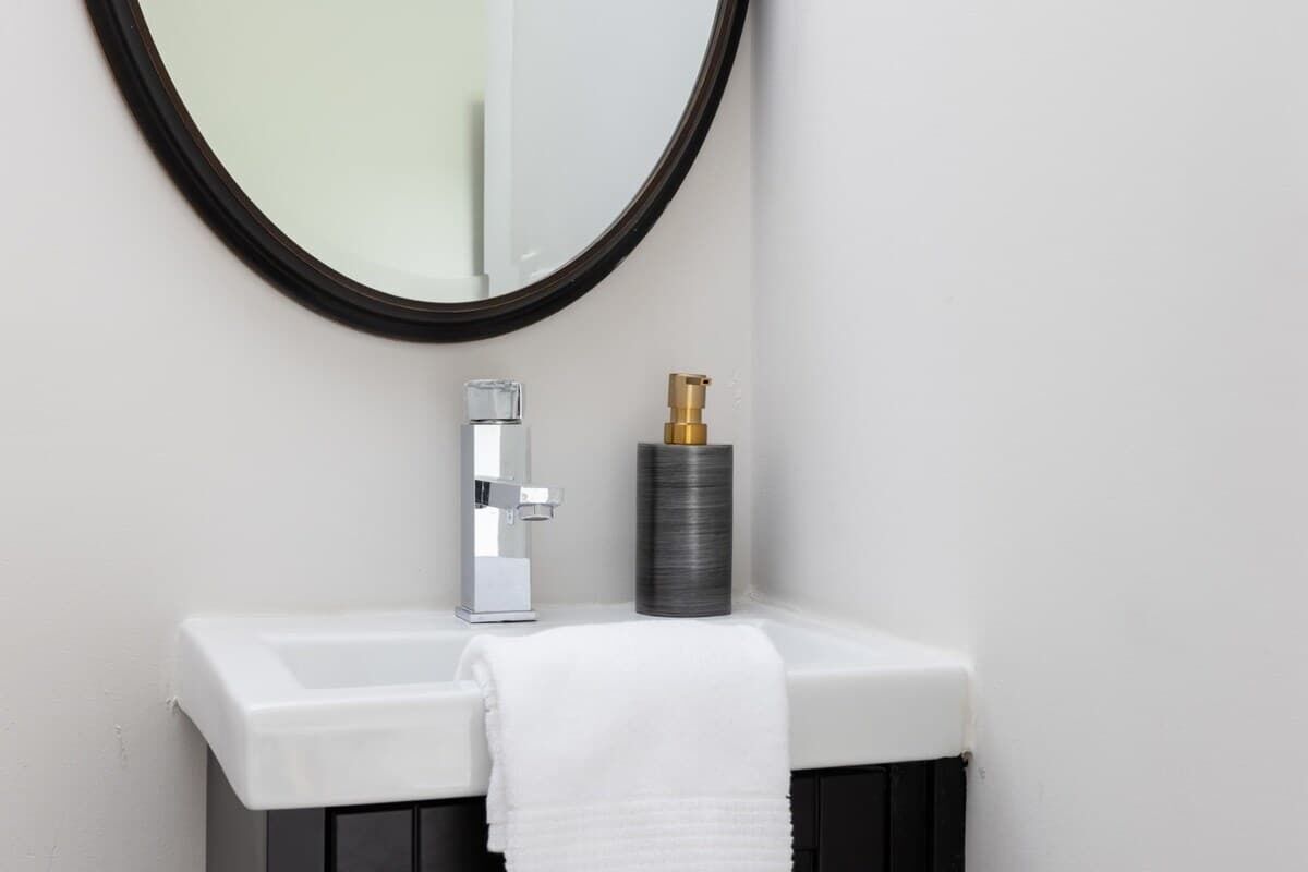 Une salle de bain avec un lavabo blanc, un robinet chromé, un miroir rond et une serviette noire.