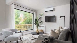 En moderne stue med stort vindue, fladskærms-tv, sofa, sofabord og et lille bord.