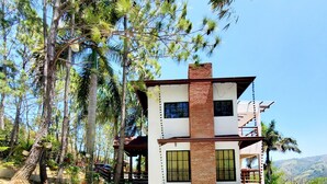 Um edifício de dois andares com piscina, cercado por árvores e uma paisagem montanhosa.