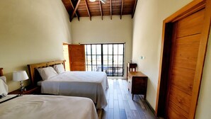 Quarto com duas camas, soalho em madeira, ventilador de teto e uma janela grande.