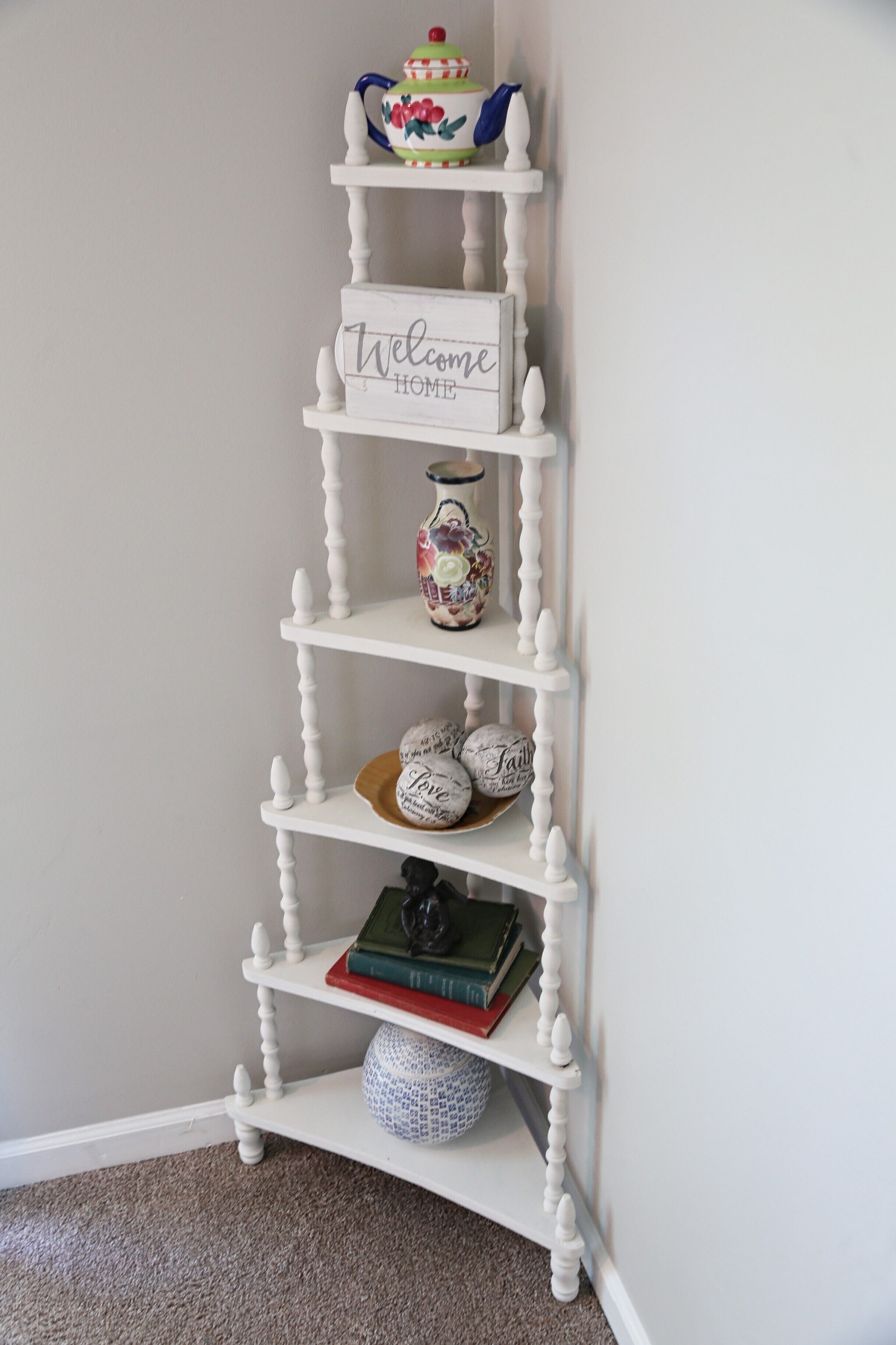 A white, multi-tiered sideboard with a 'Welcome Home' sign, decorative items, and books.