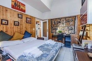 A hotel room with a wooden wall, a bed with white linens, a desk with a computer, and artwork on the walls. - GuestHost - Cozy apartment of 70 sqm, able to accommodate up to 4 people, located on the ground floor of a building with private entrance (two steps to access it).The location is enviable, in the center of Pisa, a few steps from Piazza dei Miracoli and t (Pisa)