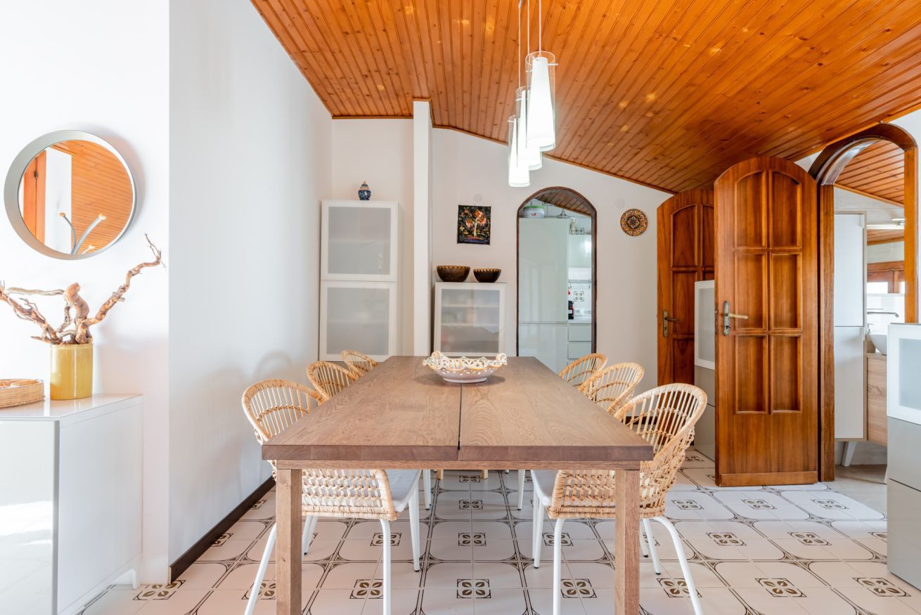 Un comedor con una mesa de madera, sillas de mimbre y una lámpara colgante.