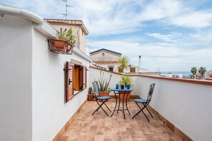 A balcony with a table and chairs, potted plants, and a view of the sea.