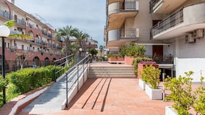 Un edificio residencial de varios pisos con balcones, una escalera y un camino bordeado de macetas.
