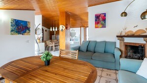 Techo de madera, una mesa redonda de madera con una planta en maceta, un sofá azul y una chimenea.