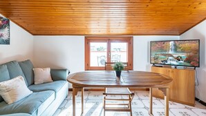 Una habitación con techo de madera, una mesa de comedor con sillas, un sofá, un televisor y una ventana con vistas a un jardín.