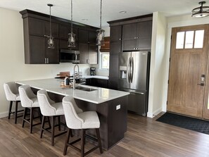 A modern kitchen with dark cabinetry, stainless steel appliances, and a central island with bar stools.
