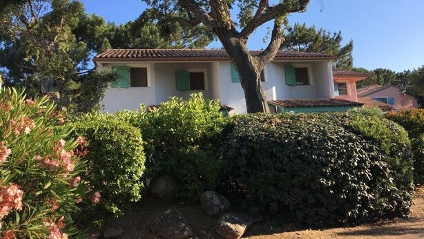Une maison à deux étages, avec un toit en tuiles, entourée de verdure et d’un grand arbre.